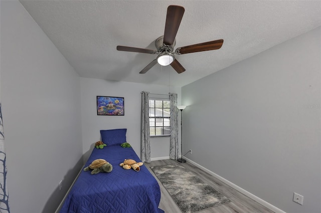 bedroom featuring a textured ceiling, wood finished floors, a ceiling fan, and baseboards