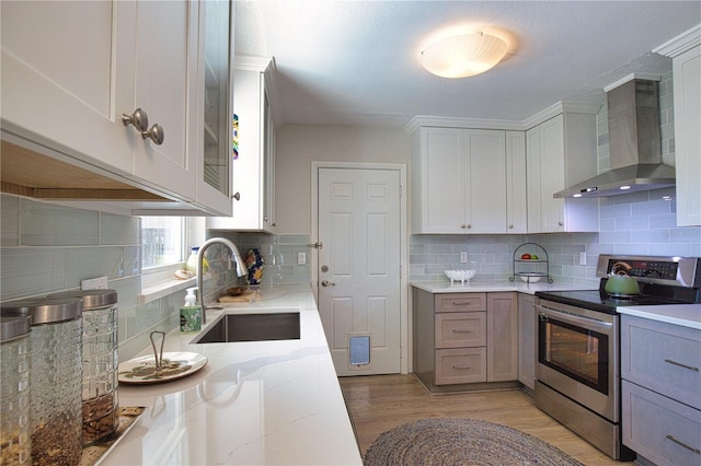 kitchen featuring decorative backsplash, wall chimney exhaust hood, light stone countertops, stainless steel range with electric stovetop, and a sink