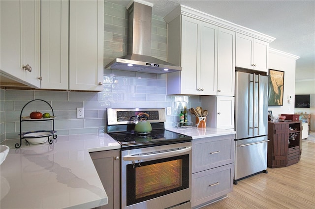 kitchen featuring crown molding, stainless steel appliances, tasteful backsplash, light wood-style flooring, and wall chimney exhaust hood