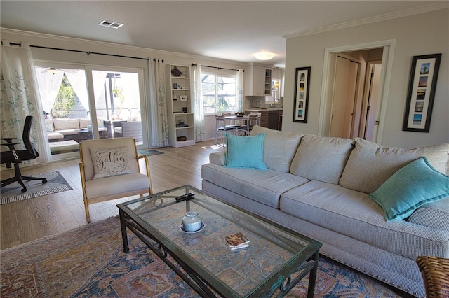 living area featuring ornamental molding, visible vents, and light wood finished floors