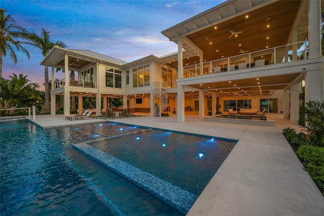 pool at dusk with a pool with connected hot tub, outdoor lounge area, stairway, a ceiling fan, and a patio area