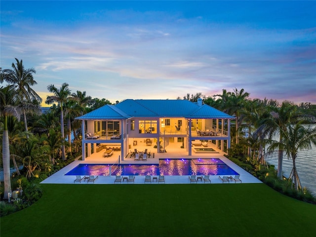 back of house at dusk with an outdoor pool, a patio area, a yard, and a balcony