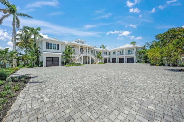 raised beach house featuring a garage, decorative driveway, a porch, and stairs