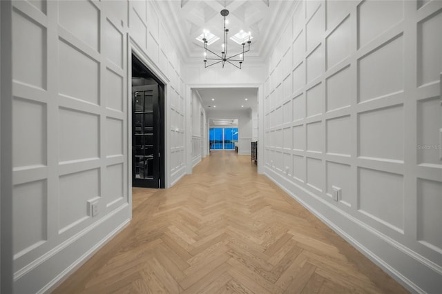 hall with a notable chandelier, crown molding, a decorative wall, a towering ceiling, and coffered ceiling