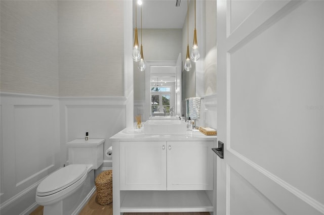 bathroom with a wainscoted wall, vanity, toilet, and a decorative wall