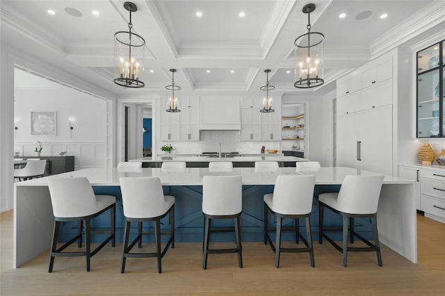 kitchen with white cabinets, light countertops, light wood-type flooring, a large island with sink, and custom range hood