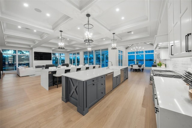 kitchen with light countertops, stainless steel dishwasher, open floor plan, a chandelier, and a large island with sink