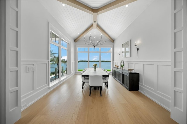 dining space with built in shelves, light wood finished floors, a water view, a decorative wall, and a chandelier