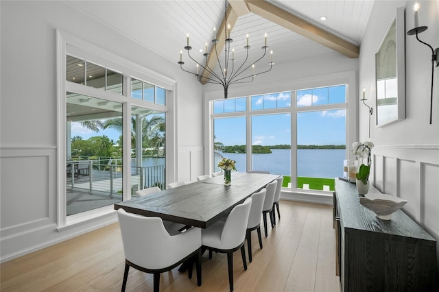 dining area with a decorative wall, a water view, light wood-type flooring, beamed ceiling, and an inviting chandelier