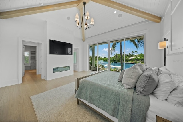 bedroom with a glass covered fireplace, beamed ceiling, access to outside, light wood-type flooring, and a notable chandelier