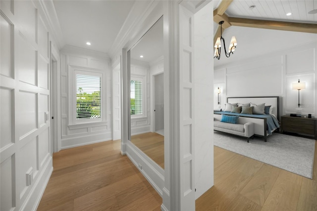 bedroom with a notable chandelier, a decorative wall, light wood-style floors, vaulted ceiling, and ornamental molding