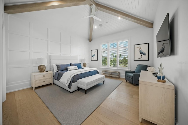 bedroom with lofted ceiling with beams, light wood-style flooring, and a decorative wall