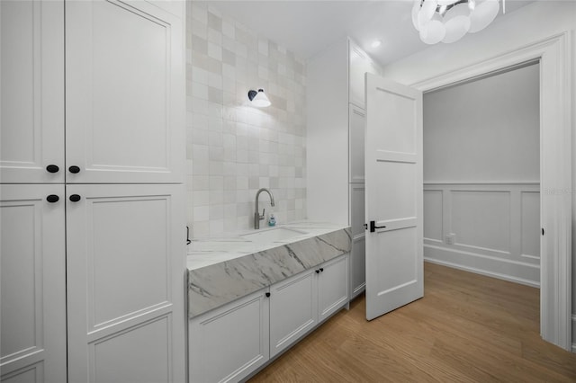 bathroom with decorative backsplash, a wainscoted wall, wood finished floors, vanity, and a decorative wall