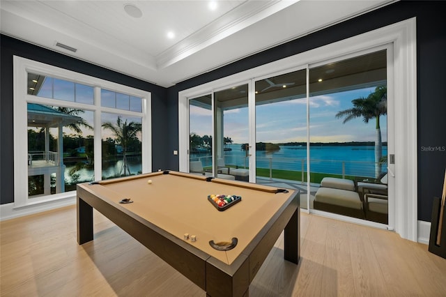 rec room with a water view, visible vents, light wood finished floors, a tray ceiling, and crown molding