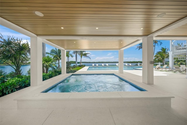 outdoor pool with a patio area, an in ground hot tub, and a water view