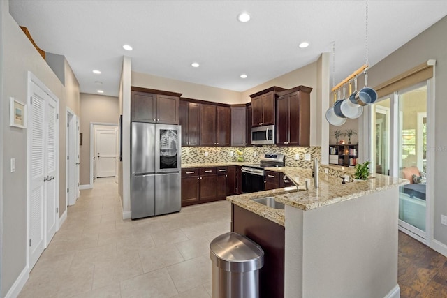 kitchen featuring a peninsula, dark brown cabinets, appliances with stainless steel finishes, backsplash, and light stone countertops