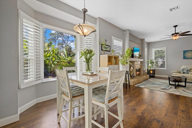 dining space featuring a healthy amount of sunlight, wood-type flooring, visible vents, and a tiled fireplace