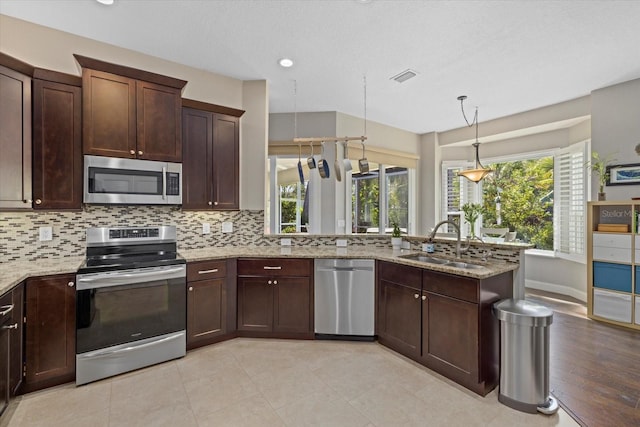 kitchen with stainless steel appliances, a sink, light stone counters, and decorative backsplash