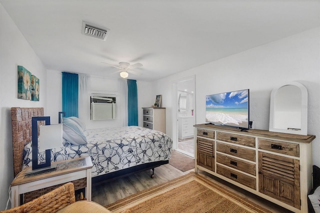 bedroom with a ceiling fan, visible vents, ensuite bathroom, and wood finished floors