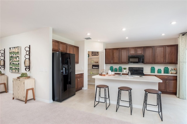 kitchen with a breakfast bar, a sink, visible vents, light countertops, and black appliances