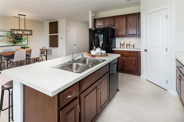 kitchen with a breakfast bar, a sink, light countertops, black appliances, and a center island with sink