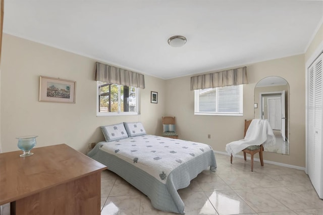 bedroom with light tile patterned floors, crown molding, baseboards, and a closet