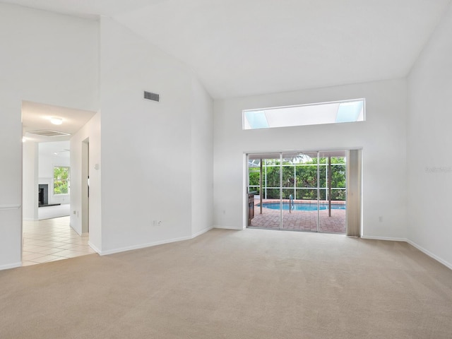 carpeted empty room featuring a fireplace with raised hearth, high vaulted ceiling, visible vents, baseboards, and tile patterned floors