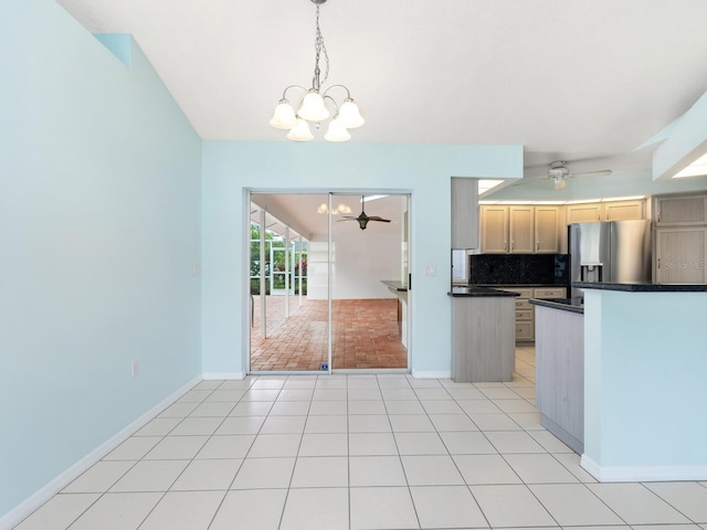 kitchen featuring light tile patterned floors, dark countertops, backsplash, stainless steel fridge, and ceiling fan with notable chandelier