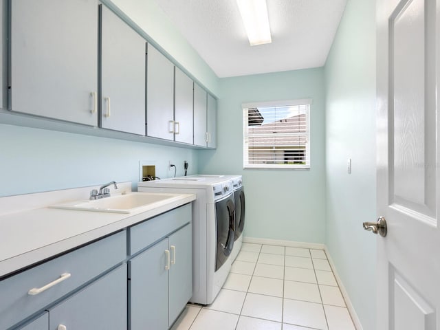 clothes washing area with cabinet space, light tile patterned floors, baseboards, washer and dryer, and a sink