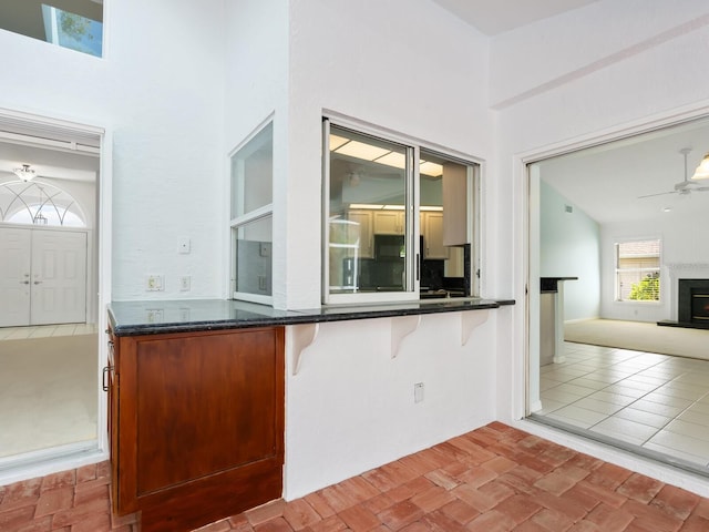 kitchen with brick floor, a breakfast bar, a fireplace with raised hearth, a ceiling fan, and open floor plan