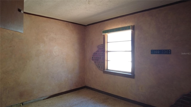 spare room featuring ornamental molding, a textured ceiling, and baseboards