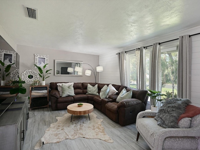 living area with visible vents, wood walls, a textured ceiling, and light wood finished floors