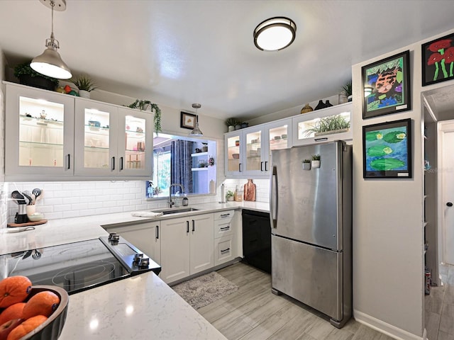 kitchen featuring a sink, white cabinets, light wood-style floors, freestanding refrigerator, and decorative backsplash