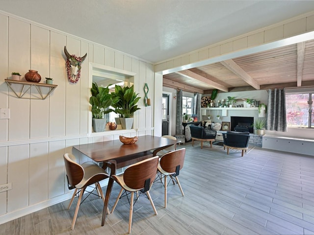 dining area featuring beamed ceiling, a fireplace, wood finished floors, and a decorative wall