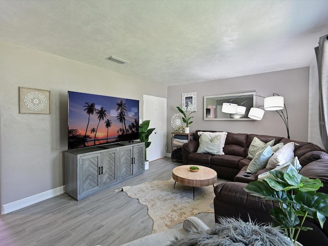 living room featuring light wood-style floors, visible vents, a textured ceiling, and baseboards