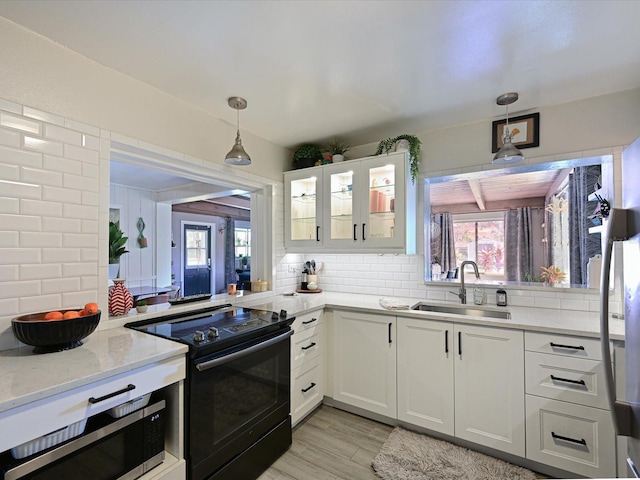 kitchen featuring glass insert cabinets, stainless steel microwave, backsplash, black range with electric stovetop, and a sink