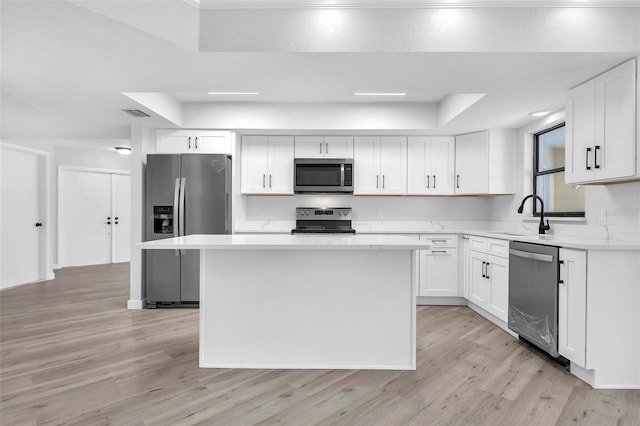 kitchen with a kitchen island, stainless steel appliances, light countertops, white cabinetry, and a sink