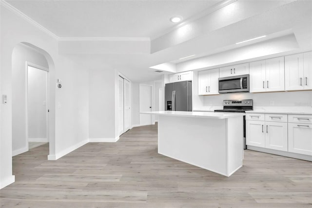 kitchen featuring arched walkways, stainless steel appliances, a kitchen island, light countertops, and ornamental molding