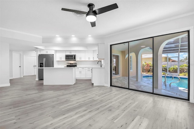 kitchen with stainless steel appliances, white cabinets, open floor plan, light countertops, and light wood-type flooring