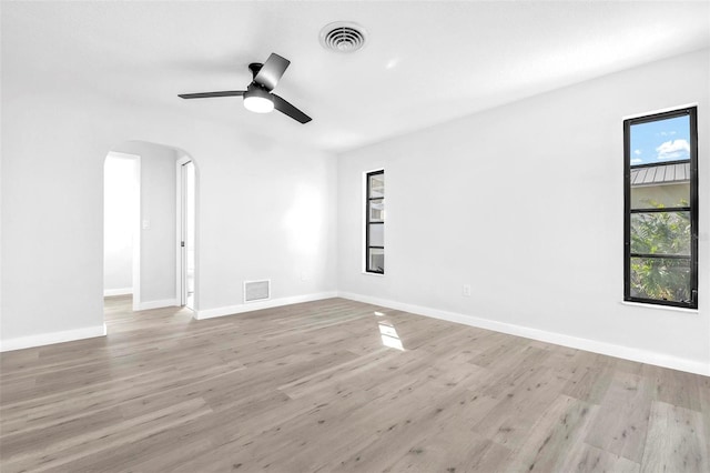 unfurnished room with light wood-style floors, arched walkways, and visible vents