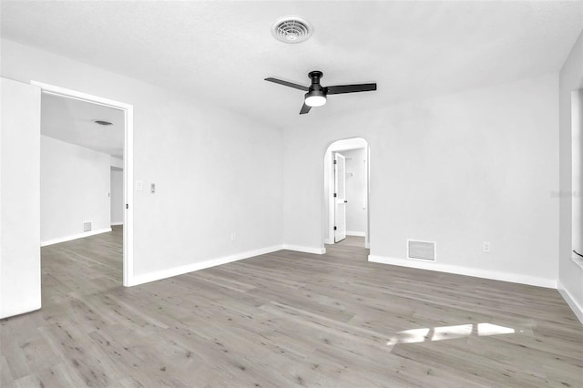 empty room with a ceiling fan, visible vents, arched walkways, and wood finished floors