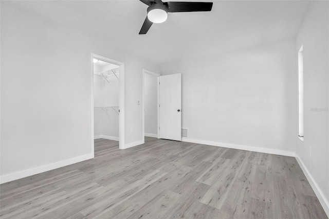 unfurnished bedroom featuring a walk in closet, a closet, ceiling fan, wood finished floors, and baseboards