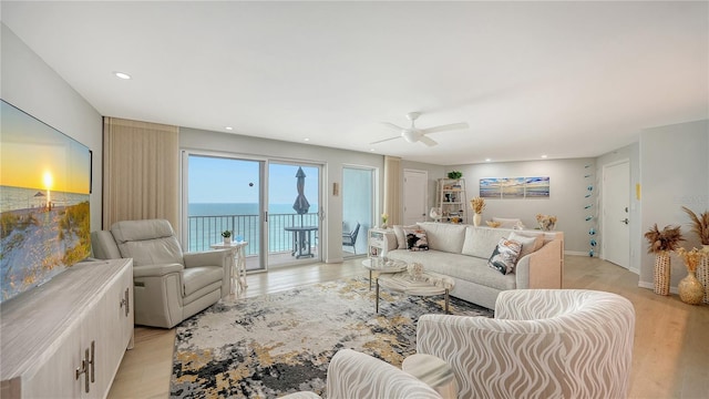 living room with recessed lighting, a water view, a ceiling fan, light wood-type flooring, and baseboards