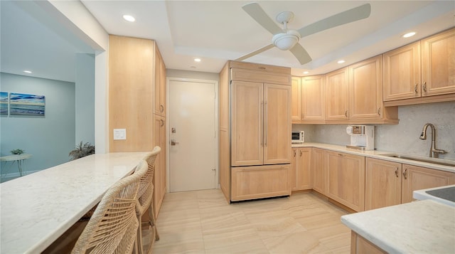 kitchen featuring recessed lighting, light countertops, decorative backsplash, light brown cabinetry, and a sink