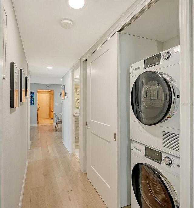 laundry area featuring stacked washer and dryer, laundry area, baseboards, and light wood finished floors