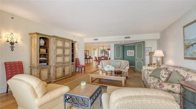 living room featuring an inviting chandelier, light wood-style flooring, and visible vents