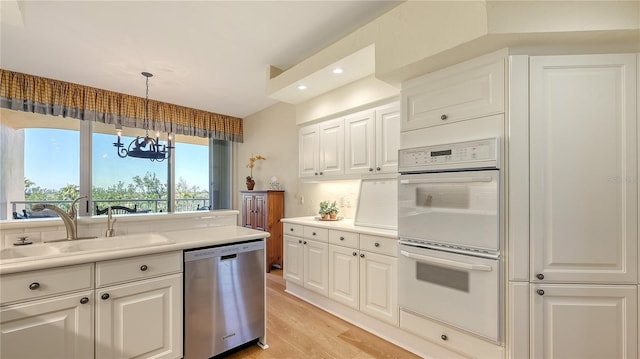 kitchen with dishwasher, white cabinetry, white double oven, and a sink