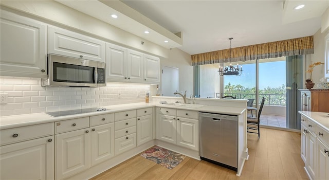 kitchen with a sink, backsplash, appliances with stainless steel finishes, a peninsula, and light wood finished floors