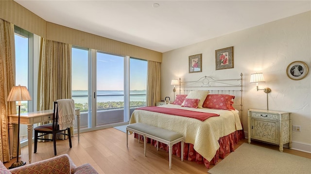 bedroom featuring access to exterior, baseboards, light wood-style floors, and a water view