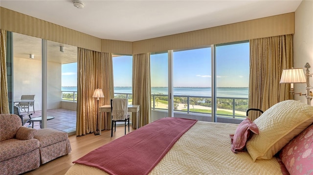 bedroom with light wood finished floors, a water view, and access to outside